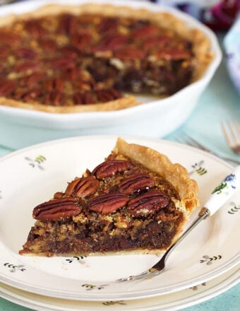 Chocolate Pecan Pie with bourbon slice on a white plate with a whole pie in the background.