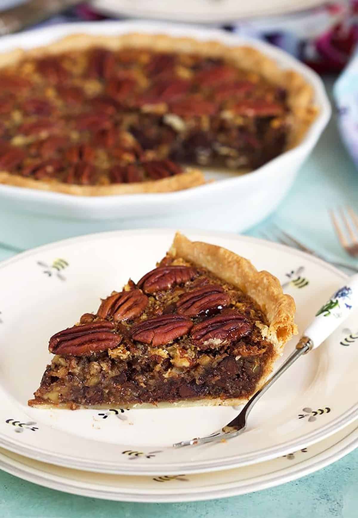 Chocolate Pecan Pie with bourbon slice on a white plate with a whole pie in the background.