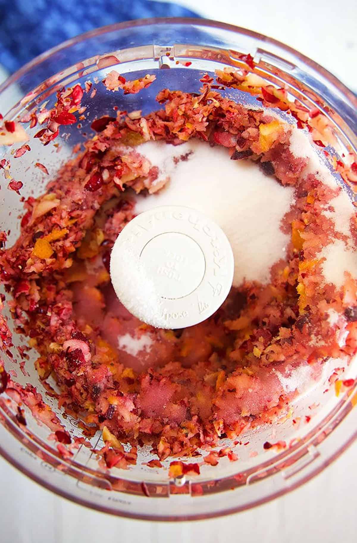 chopped ingredients for cranberry relish in the bowl of a food processor.