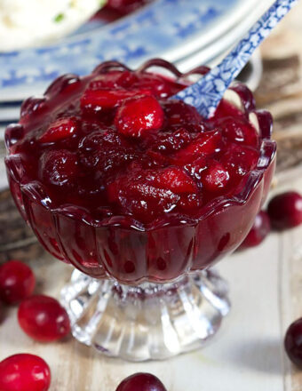 Cranberry sauce in a glass dessert bowl with a blue and white spoon.