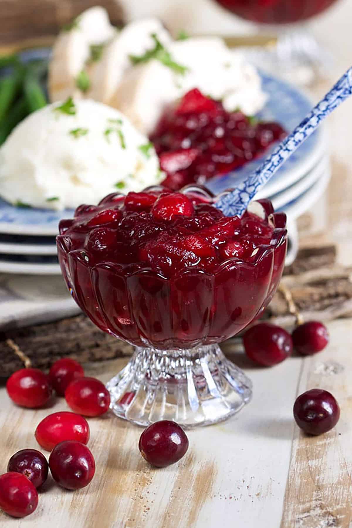 Cranberry Sauce in a compote bowl with a blue and white spoon on a distressed white wood background.