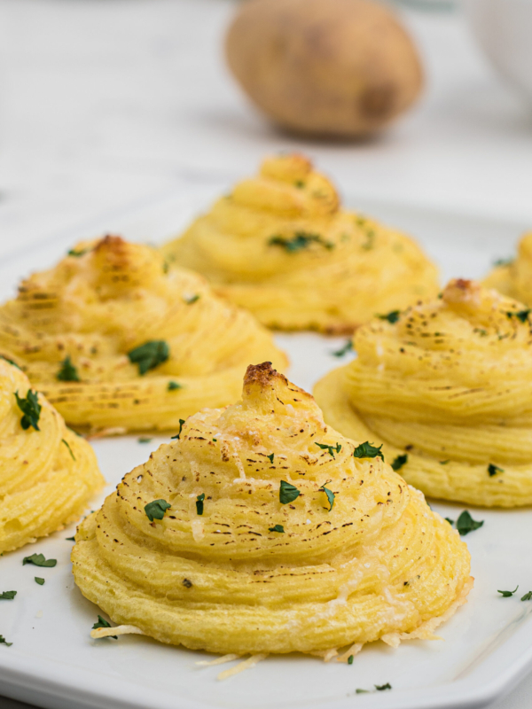 Several servings of duchess potatoes are presented on a white serving platter.