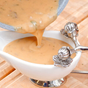 Gravy is being poured from a pot into a small white gravy dish.
