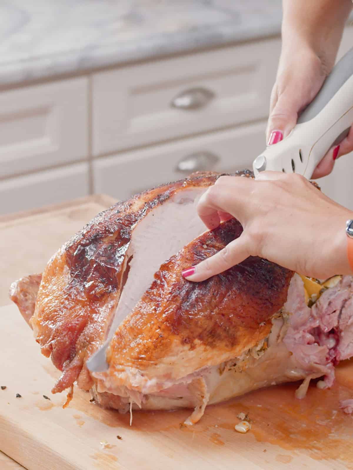Breast being cut off a roast turkey on a cutting board.