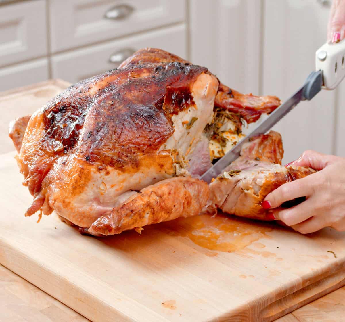 Leg being cut off a roast turkey on a cutting board with an electric knife.