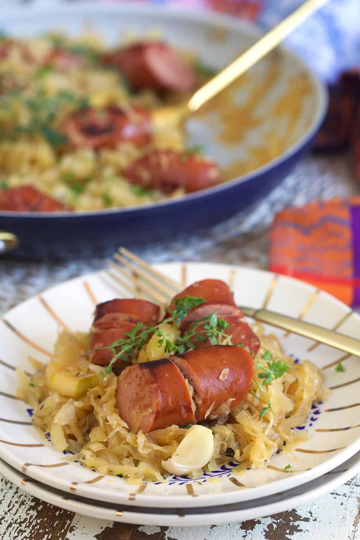 Sausage is piled on top of a serving of sauerkraut and apples on a white striped plate.