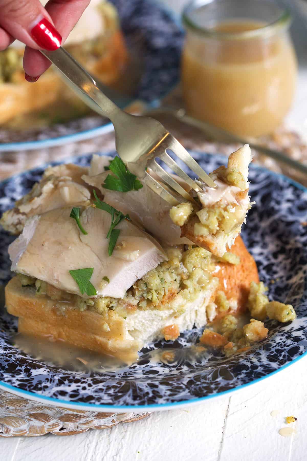 A fork is taking a bite out of an open faced turkey sandwich.