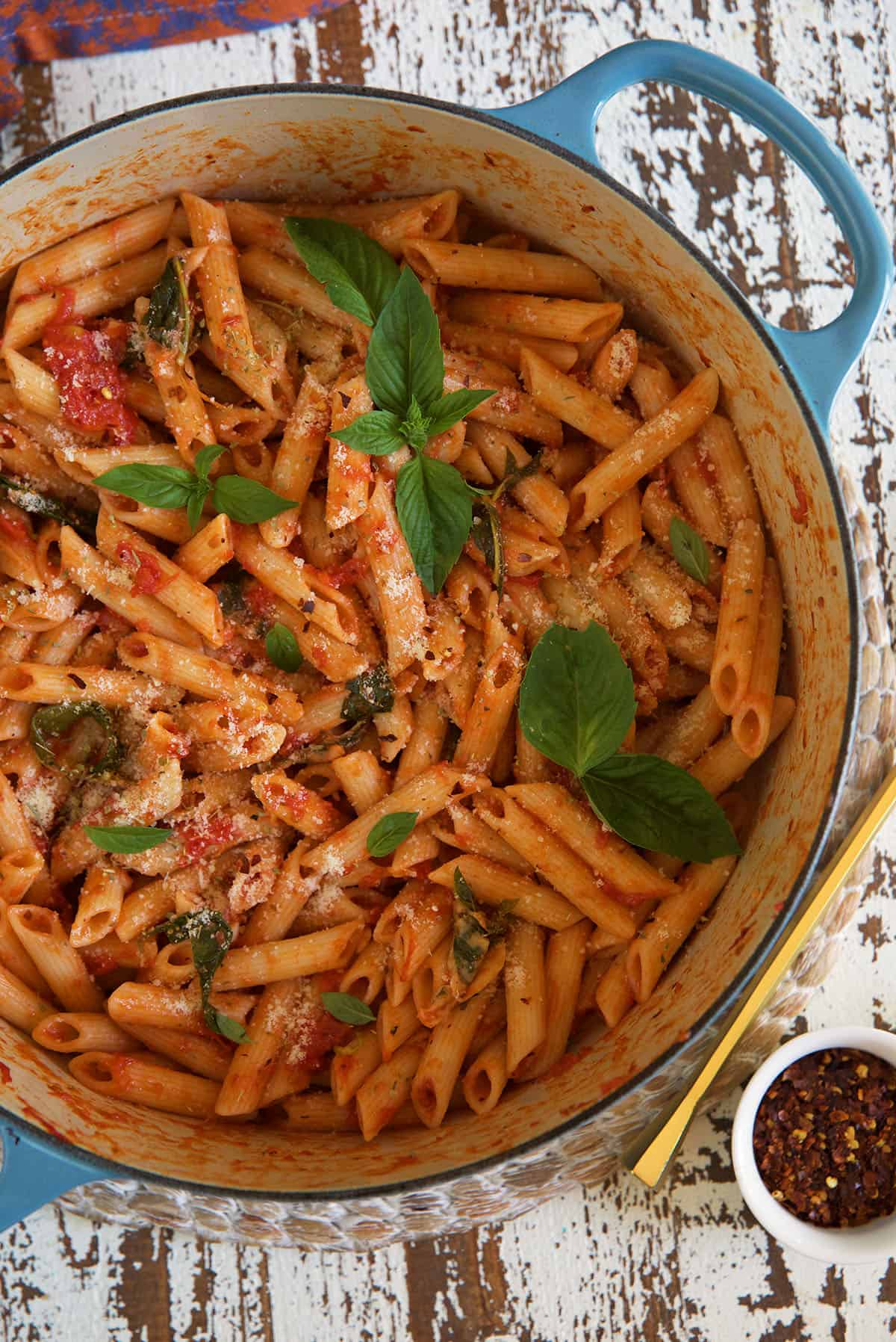 A white and blue dutch oven is filled with cooked penne pomodoro, topped with fresh basil.