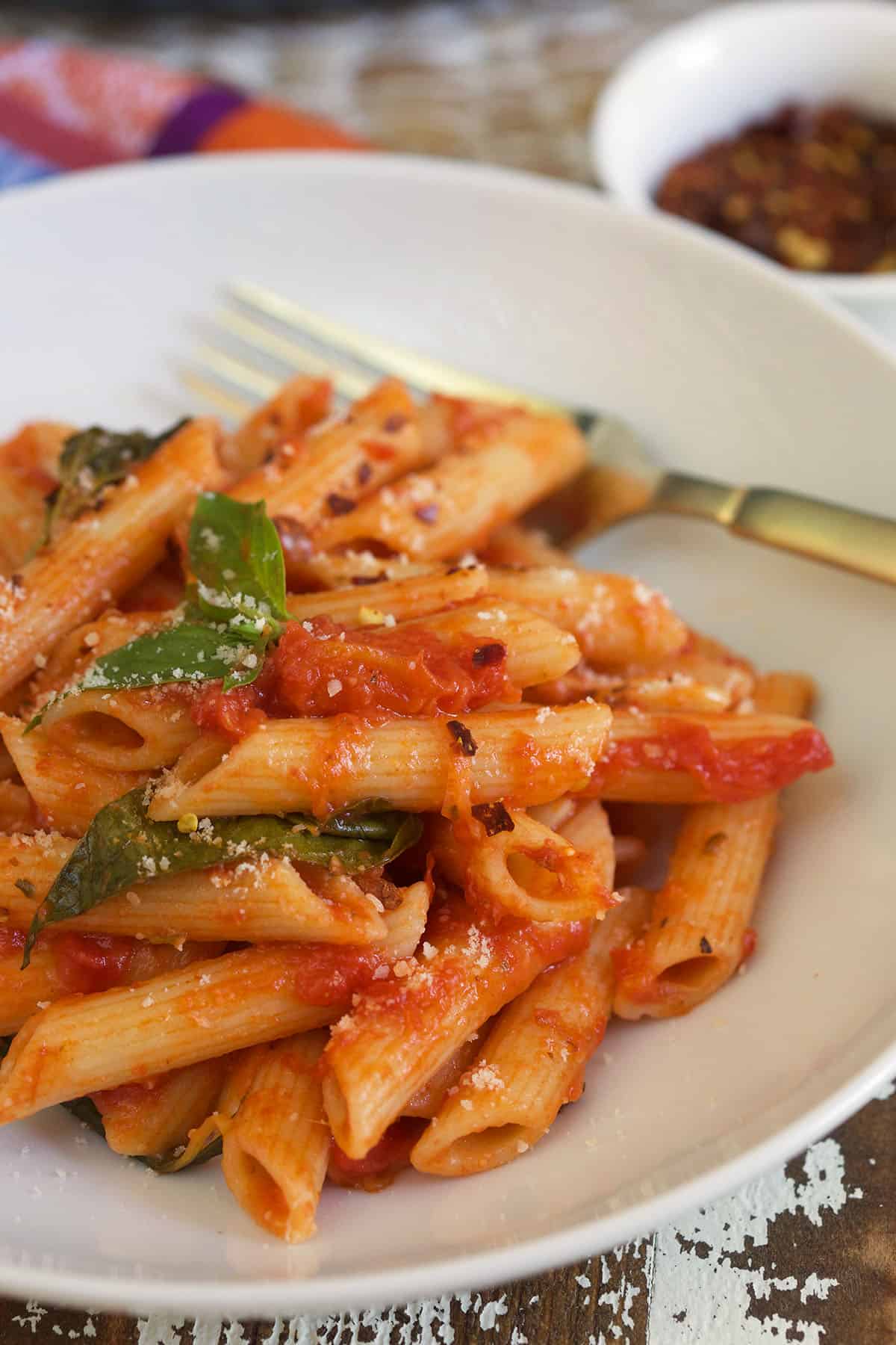 A serving of penne pomodoro is on a white plate with a fork.