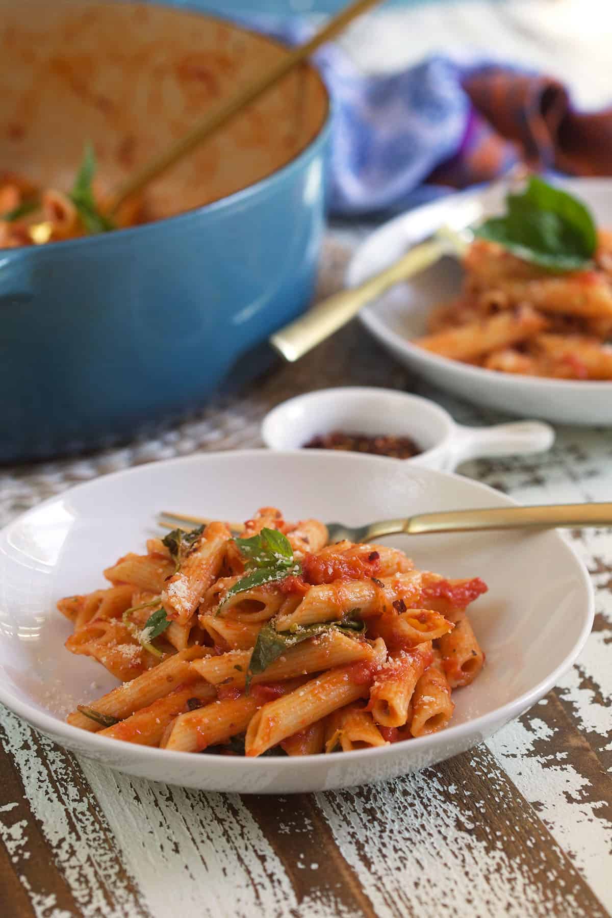 A white plate is filled with pasta pomodoro and topped with fresh basil.