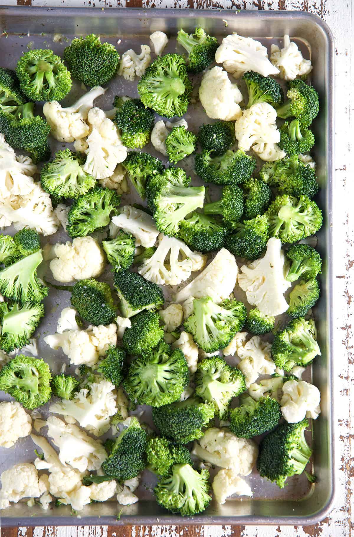 Uncooked broccoli and cauliflower are spread out on a baking sheet.