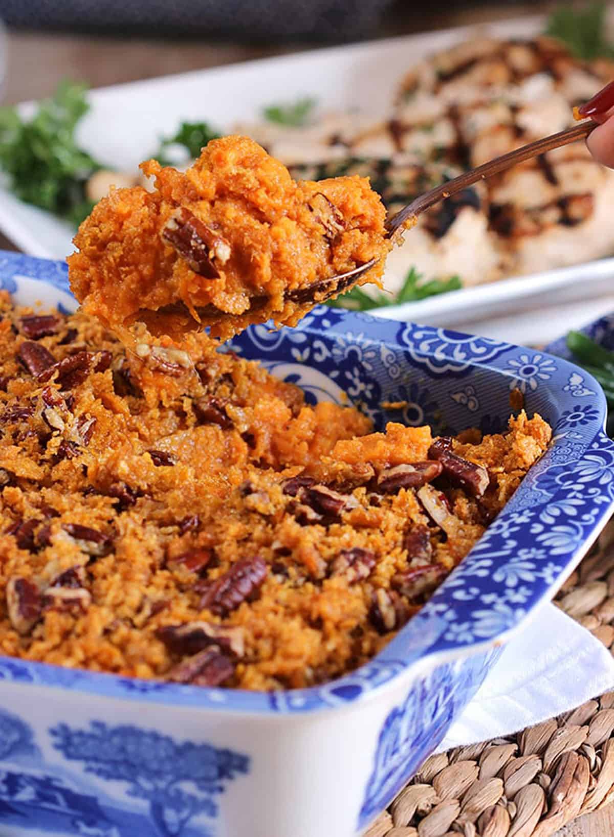 Hand with a serving spoon over a baking dish with sweet potato casserole.