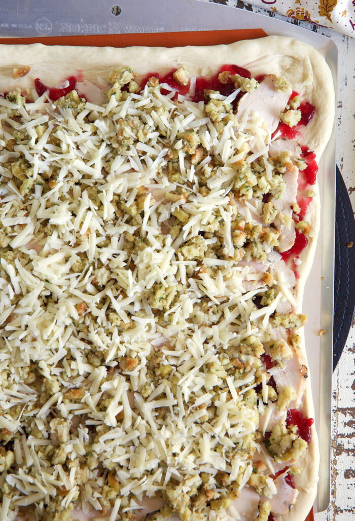 Pizza dough has been covered in cheese, stuffing, turkey, and cranberry sauce.