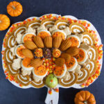 A dessert board is filled with plenty of orange and brown Thanksgiving treats in the shape of a turkey.