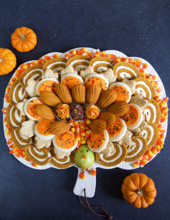 A dessert board is filled with plenty of orange and brown Thanksgiving treats in the shape of a turkey.