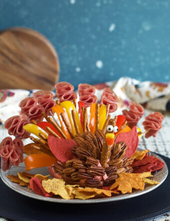 A cheese ball is decorated with sliced meats, pretzels, and more to resemble a turkey.