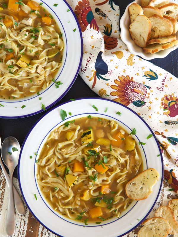 Two white bowls are filled with servings of turkey noodle soup.