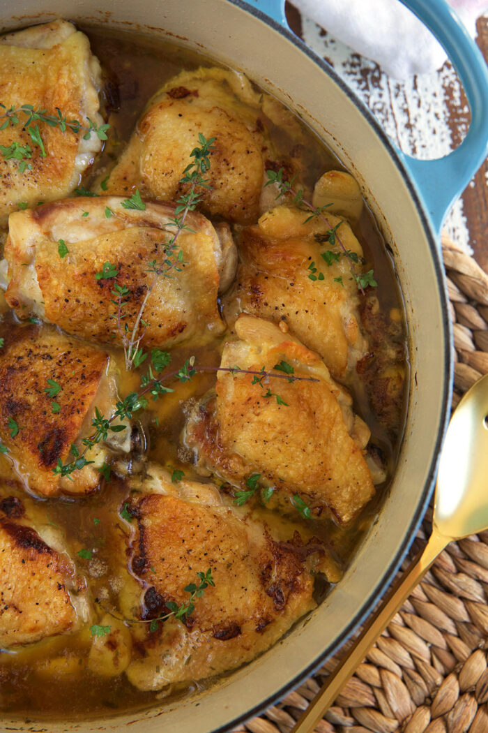 Several chicken thighs are being cooked in a large blue and white dutch oven with several other ingredients. 
