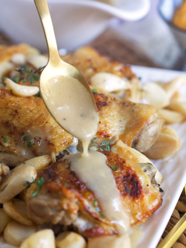 Pan sauce is being drizzled by a spoon over a cooked chicken thigh.