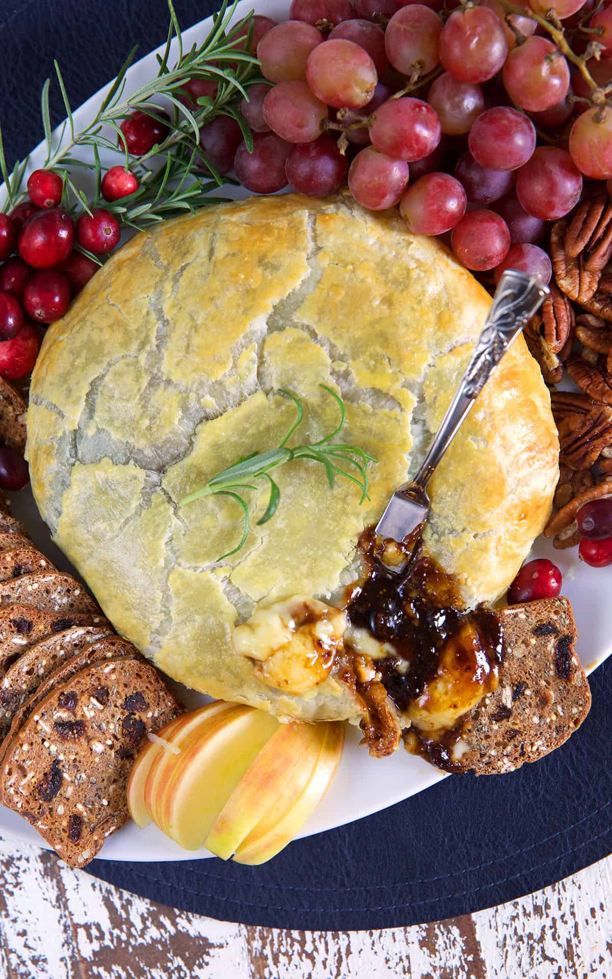 A baked wheel of brie is surrounded by grapes, bread, and more.