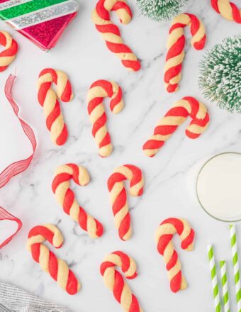 Candy Cane Cookies arranged on a marble table with green and white striped straws next to a glass of milk