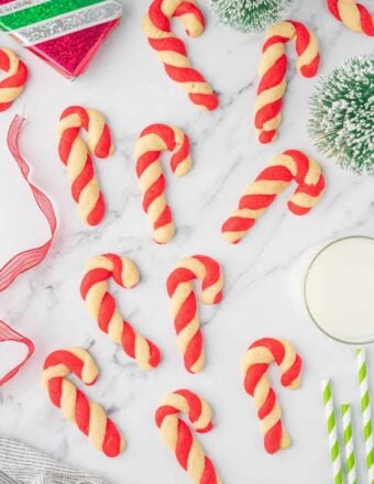 Candy Cane Cookies arranged on a marble table with green and white striped straws next to a glass of milk