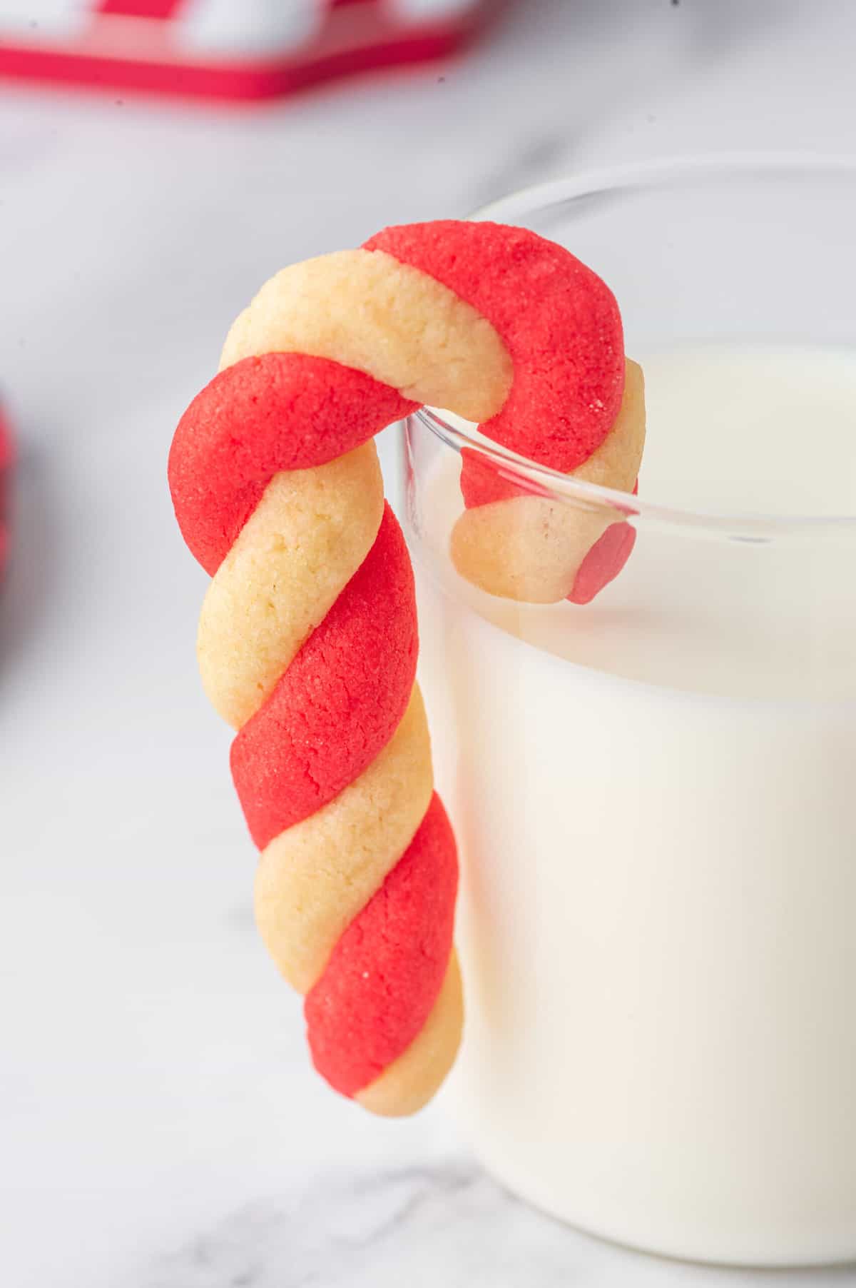 Candy Cane Cookie hanging on the side of a glass of milk.