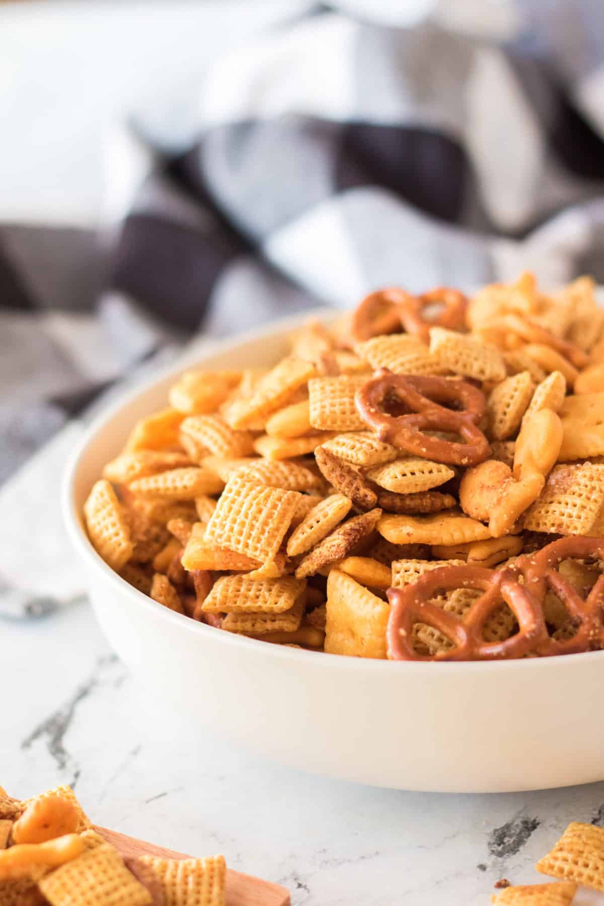 A white bowl is filled to the brim with a large serving of homemade cheddar chex mix.