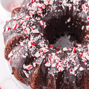 A chocolate bundt cake topped with peppermint ganache is presented on a white cake tray.