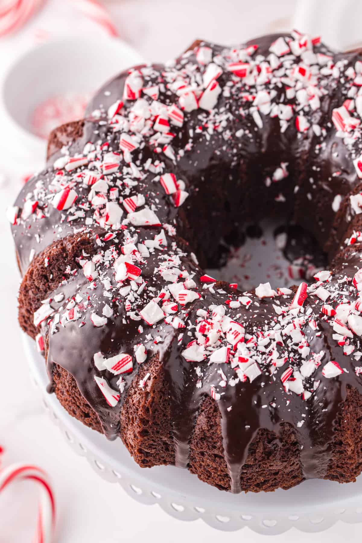 A chocolate bundt cake topped with peppermint ganache is presented on a white cake tray.