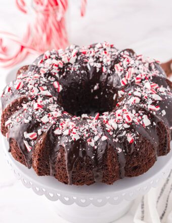 A chocolate bundt cake is topped with ganache and peppermint bits.