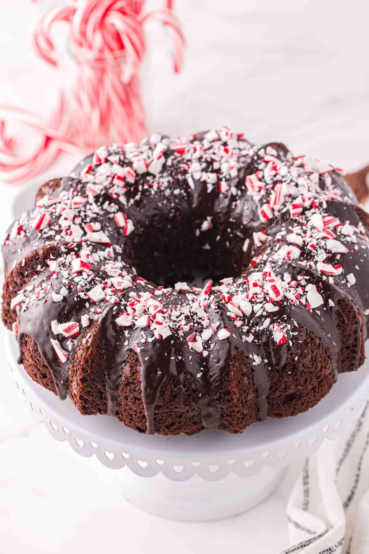 A chocolate bundt cake is topped with ganache and peppermint bits. 