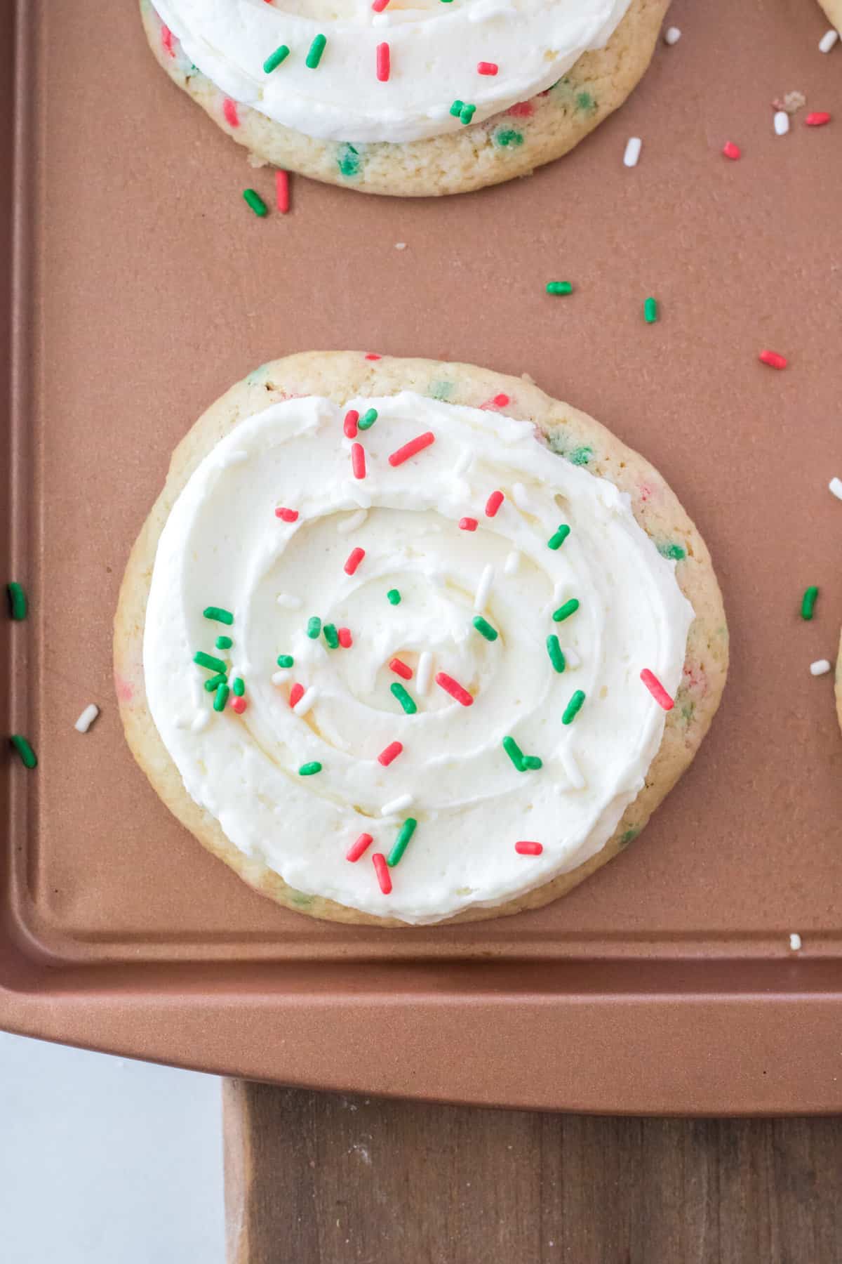 A frosted and sprinkled cookie is on a bronze baking sheet.