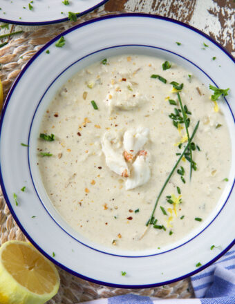 A white bowl is filled with creamy crab soup and garnished with fresh green herbs.