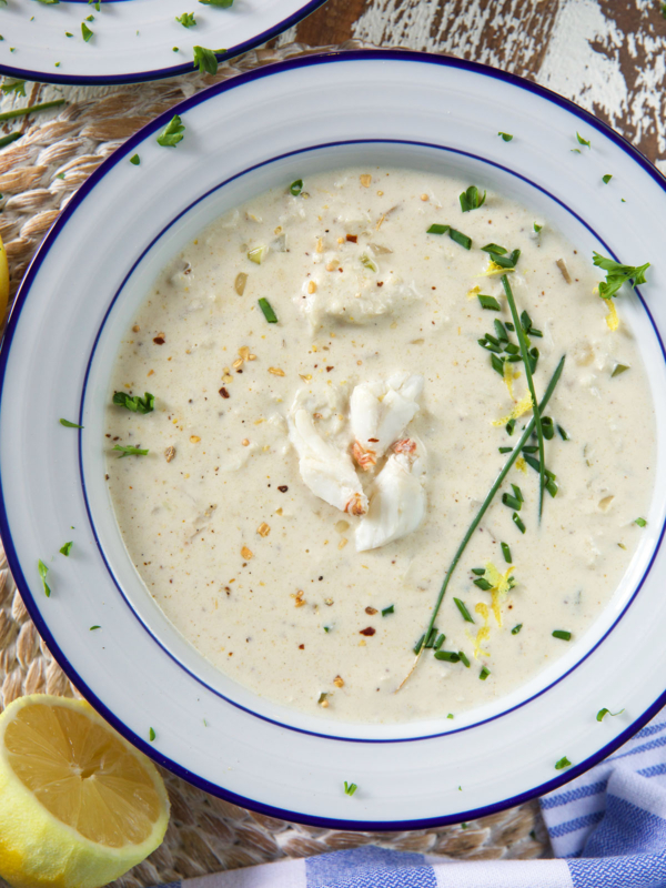 A white bowl is filled with creamy crab soup and garnished with fresh green herbs.