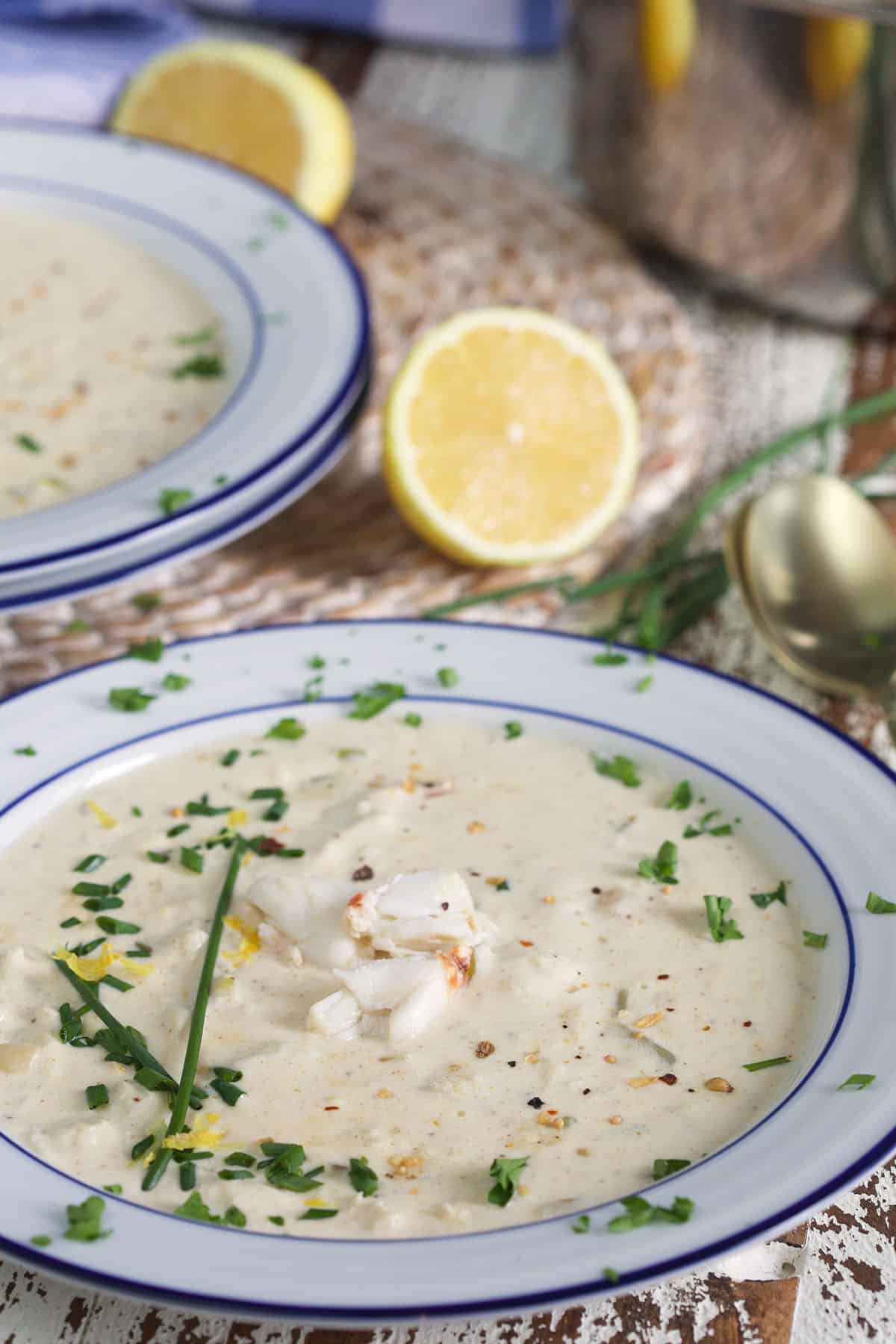 A bowl of crab soup is garnished with chives and placed next to a fresh lemon half.