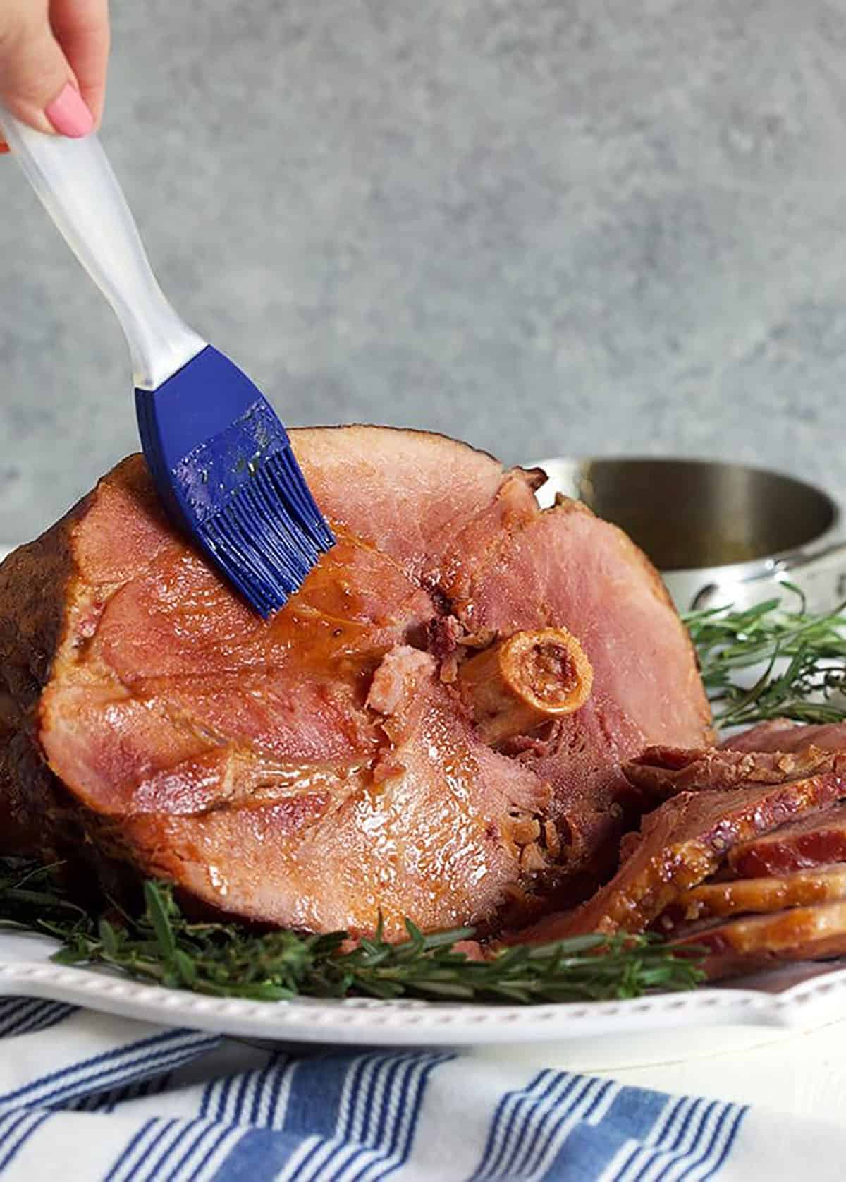 Crock Pot Ham being basted with glaze with a blue silicon basting brush.