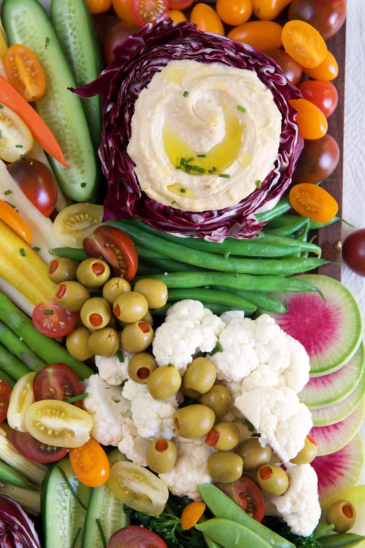 Multiple fresh veggies are placed on a platter with hummus.