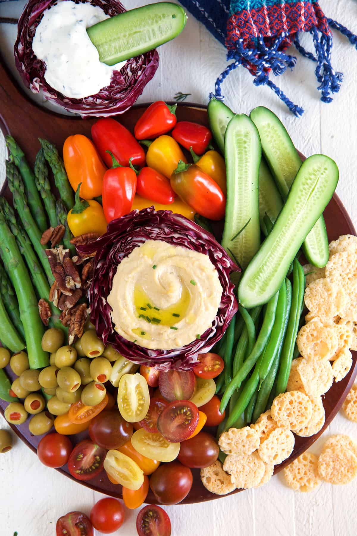 A serving of hummus is surrounded by a rainbow of various veggies on a round platter.