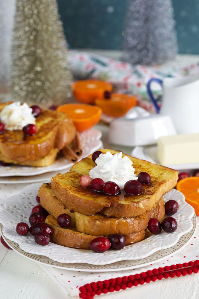 A dollop of whipped cream and cranberries are placed on a stack of eggnog french toast.