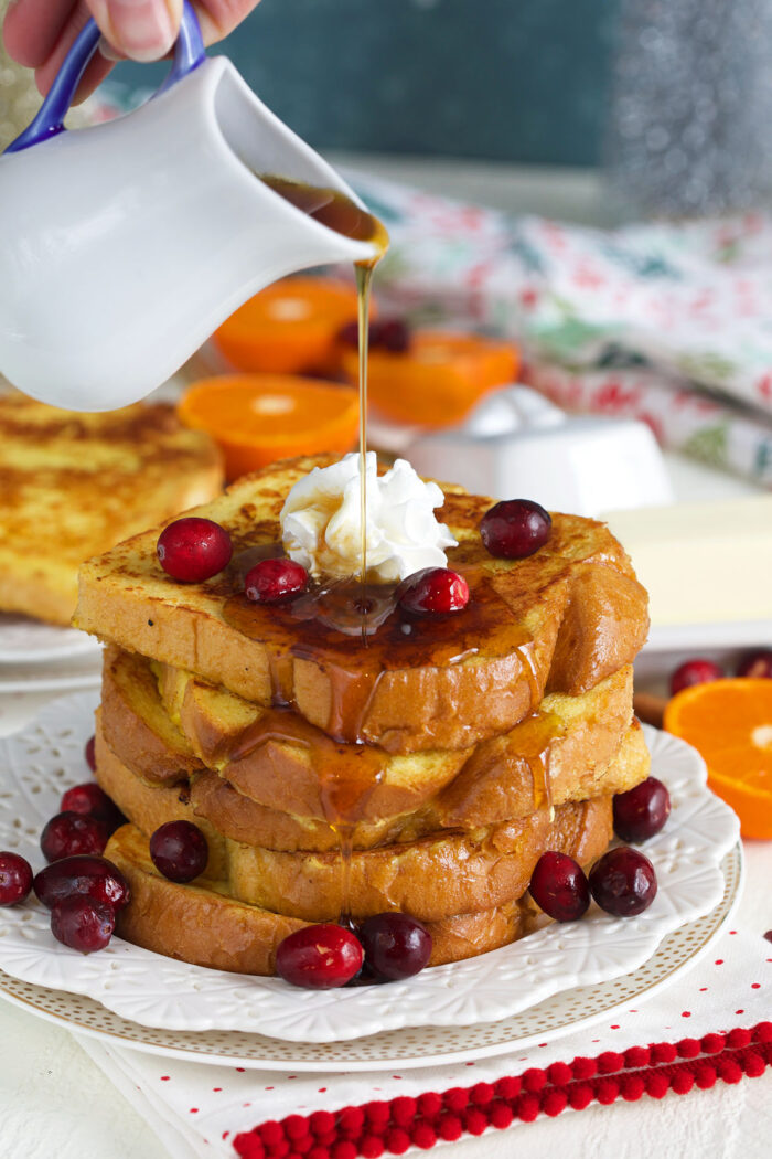 Syrup is being poured on top of a stack of french toast.