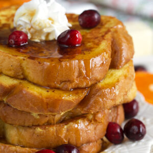 A stack of french toast is presented on a round white plate with berries and cream.