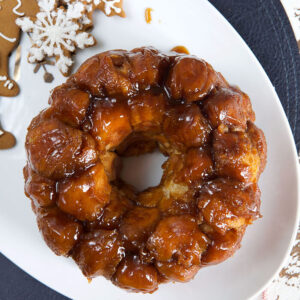 A ring of monkey bread is placed on a white platter next to gingerbread cookies.