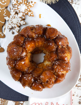 A ring of monkey bread is placed on a white platter next to gingerbread cookies.