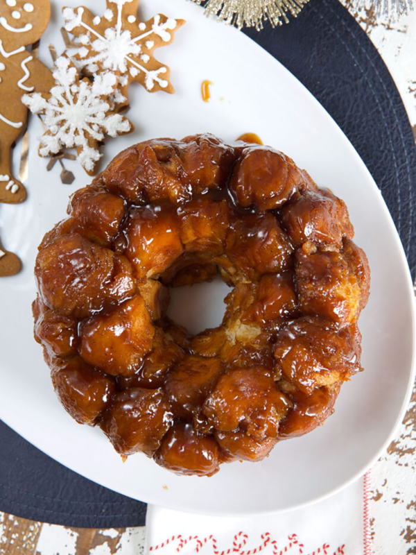 A ring of monkey bread is placed on a white platter next to gingerbread cookies.
