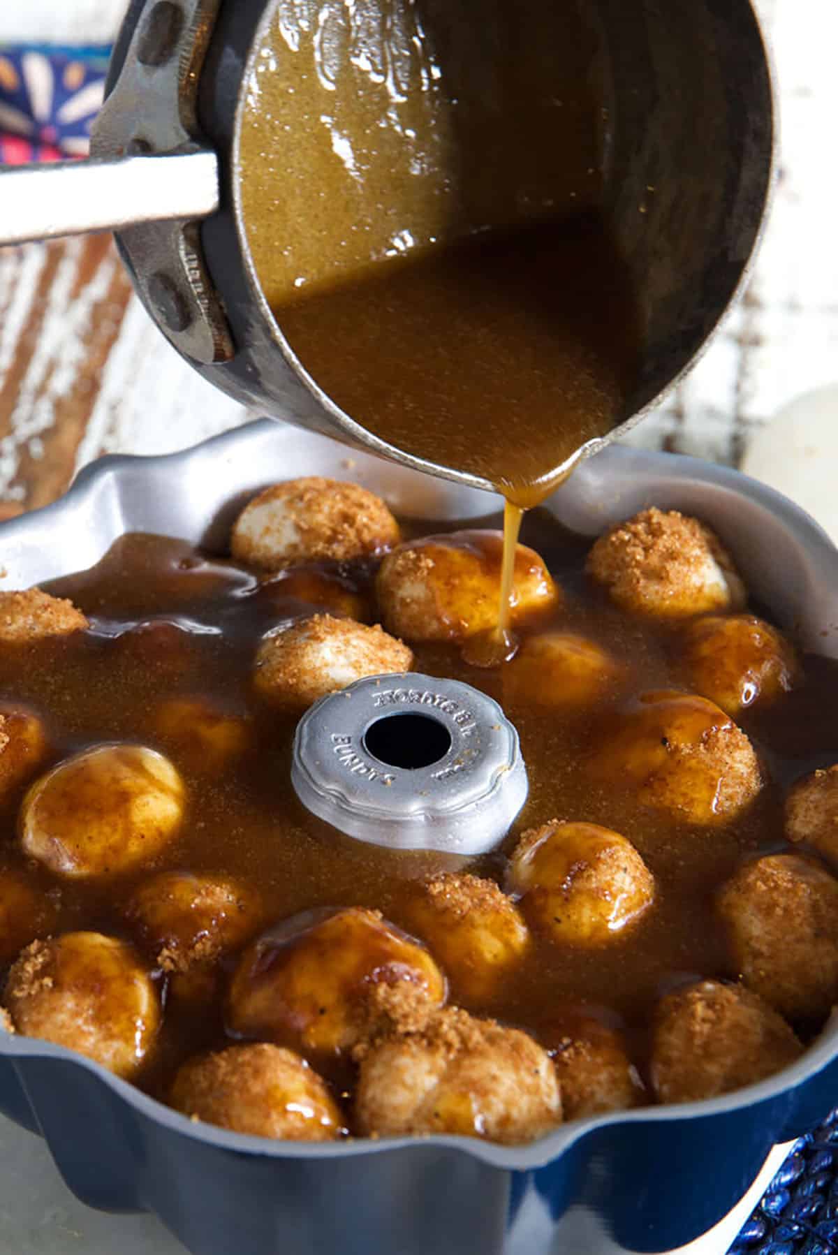 Sauce is being poured from a pot onto a ring of monkey bread.