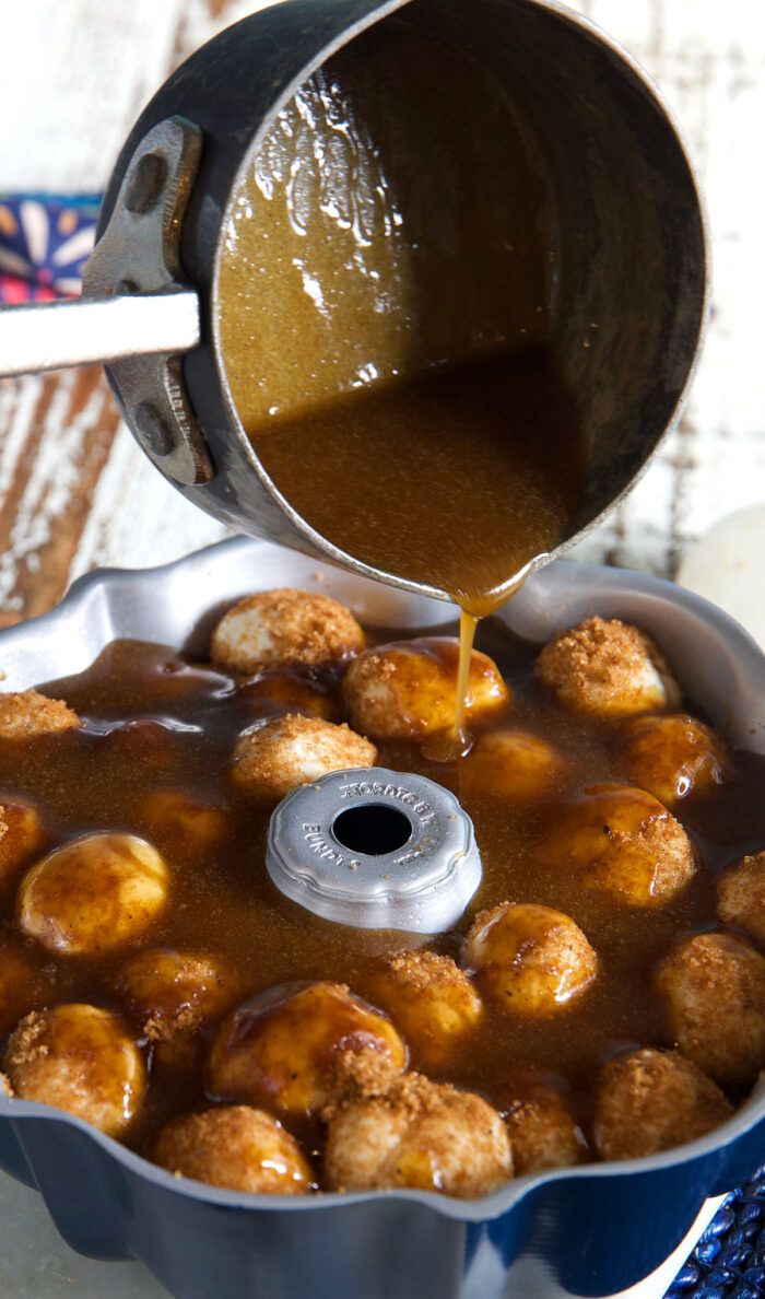 Sauce is being poured from a pot onto a ring of monkey bread.