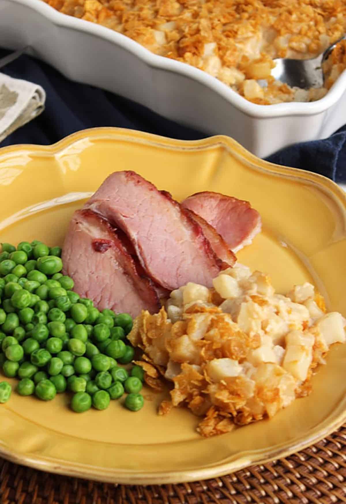 Hash Brown Casserole on a gold plate with ham slices and peas.