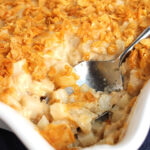 Hash Brown Casserole in a white baking dish with a spoon in for serving.
