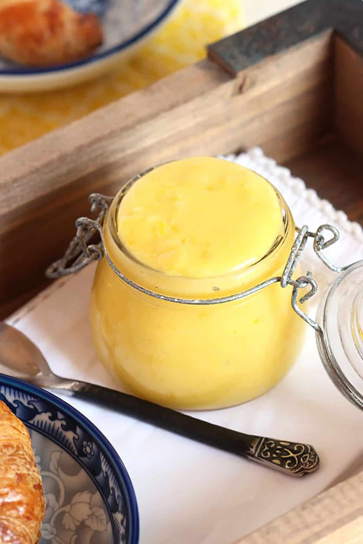 Lemon Curd in a jar on a white napkin with a spoon next to it.